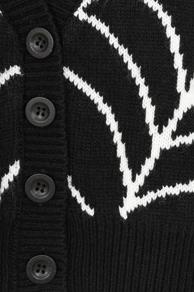 A black cropped cardigan sweater with a bright white jacquard knit-in spiderweb pattern across the chest and shoulders, featuring a V-neck and four front buttons. Shown from front in close up of spiderweb pattern detail