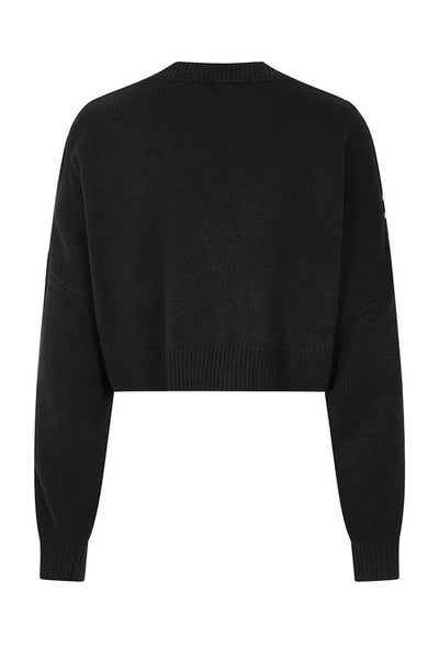 A black cropped cardigan sweater with a bright white jacquard knit-in spiderweb pattern across the chest and shoulders, featuring a V-neck and four front buttons. Shown from back