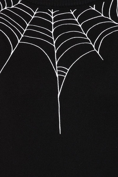 A black long-sleeve knit sweater with white embroidered spiderweb patterns across the chest and on the lower sleeves. Sweater has balloon style sleeves and ribbed neck, bottom band, and cuffs. Shown from front in close up of embroidery detail 