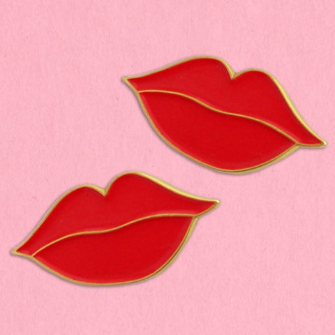 Set of two gold metal and red soft enamel pins in the shape of two sets of lips. Shown on a light pink background