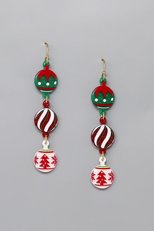 Acrylic dangle earrings in the shape of three holiday tree ornaments each connected to each other with an o ring. Glittery acrylic with a Santa hat pattern, candy cane stripes, and a red and white tree pattern