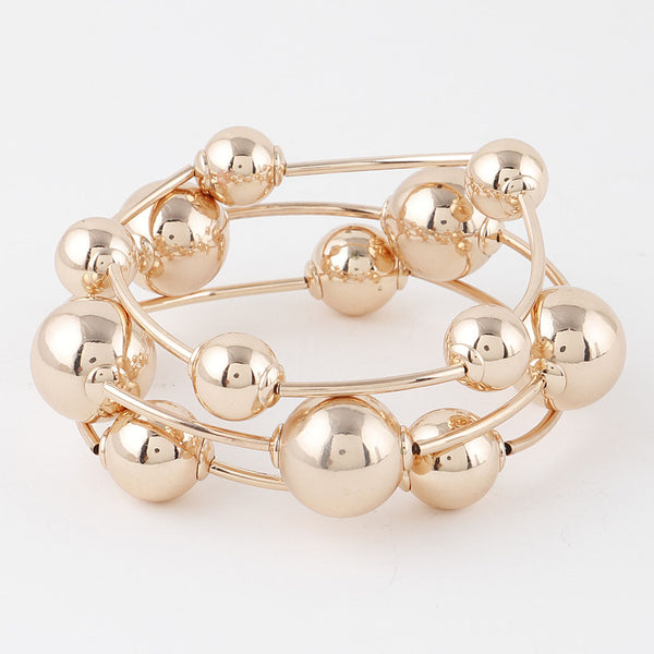 Set of three differently sized plastic metallic gold stretch bracelets with round beads in between long segments. Shown flat in set