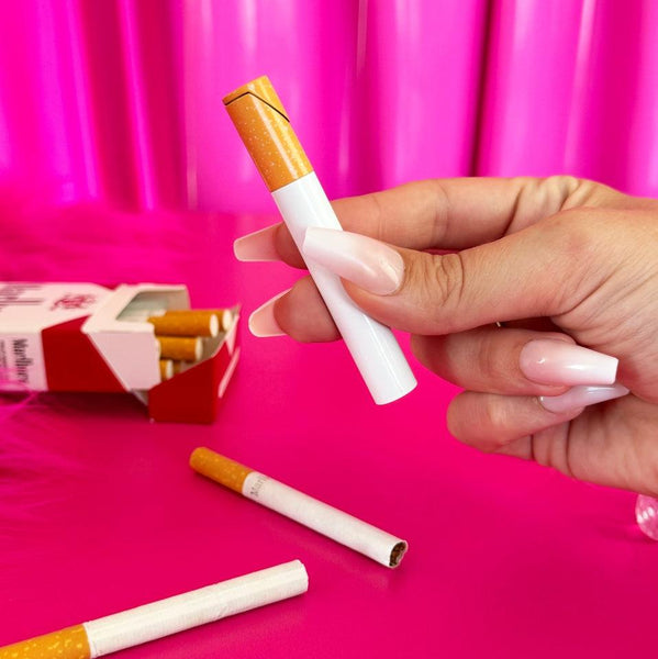 yellow and brown lighter in the shape of a cigarette. Held in front of a pink background