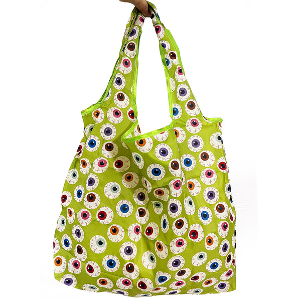 A lime green reusable nylon tote bag with an all-over pattern of large cartoonish eyeballs in various colors, held by a hand against a plain white background.