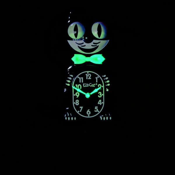 black & white glow in the dark Kit-Cat wall mount clock features a mischievous grin, and big round eyes that swivel side-to-side in time with its pendulum tail. Shown in dark with glowing bowtie and clock hands from front
