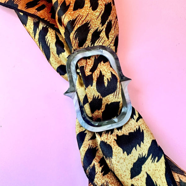 layered acrylic pearly black and grey scarf slide in the shape of an oversized chain link. Shown woven through leopard print scarf on pink background