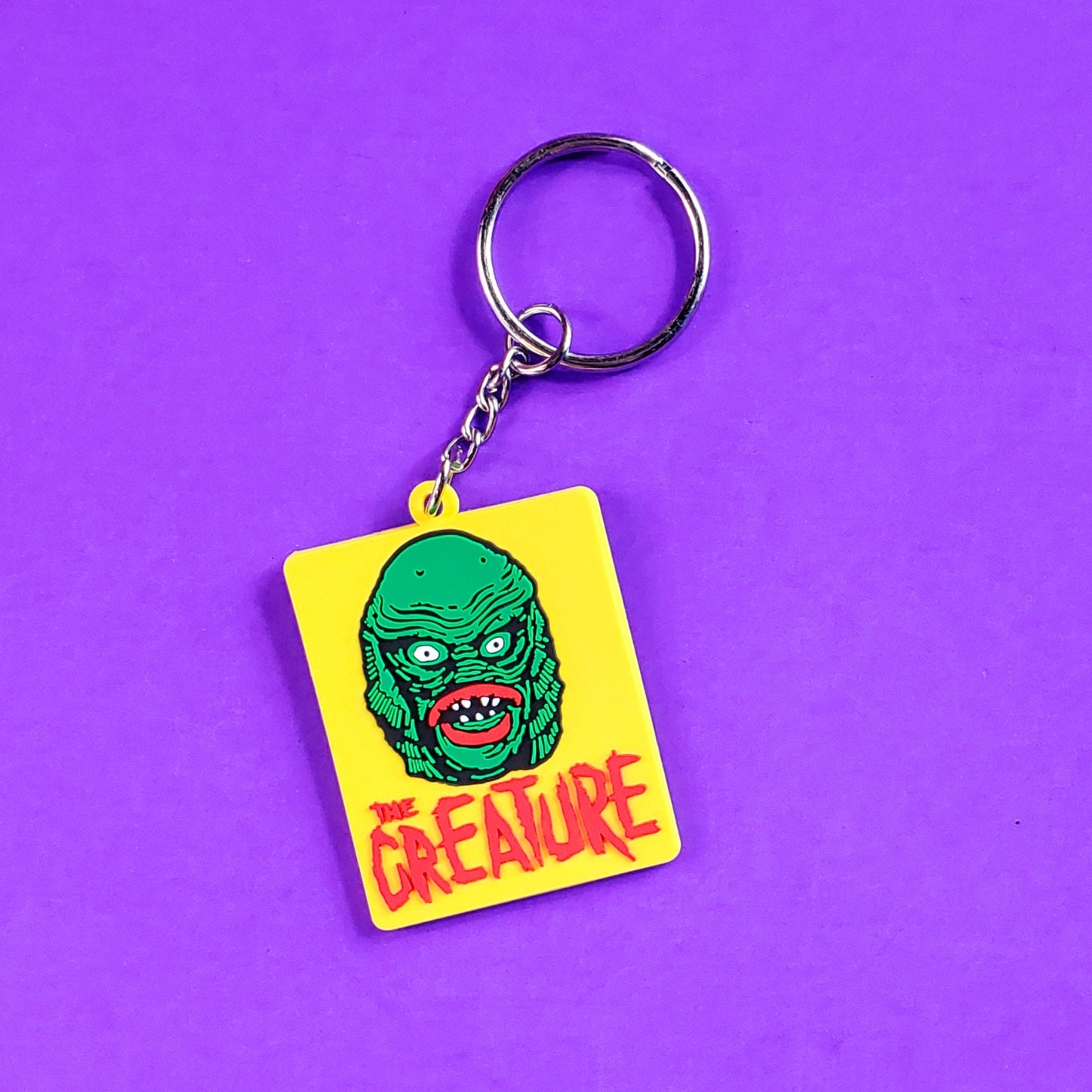 Rectangular PVC keychain of the Creature from the Black Lagoon on a bright yellow background with “THE CREATURE” written in red jagged text