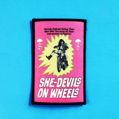 rectangular sublimated patch featuring art from the poster of the 1968 biker exploitation film She-Devils on Wheels on a neon pink background with a black border