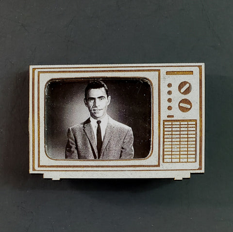 A refrigerator magnet in the shape of a vintage television in matte gray with brown details laser-cut Draftboard layered over black acrylic base, featuring Rod Sterling, the host of the classic tv show The Twilight Zone, on the screen in black and white