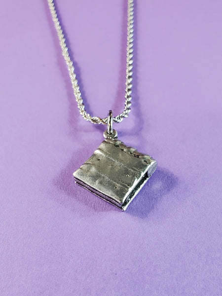American pewter charm shaped like an ancient book of spells with a large pentagram on the front. Hanging on a stainless steel rope chain. Shown from the back
