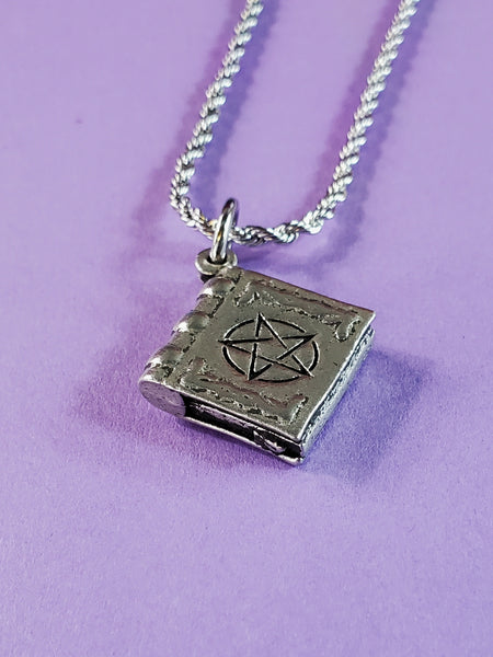 American pewter charm shaped like an ancient book of spells with a large pentagram on the front. Hanging on a stainless steel rope chain. Shown from the front