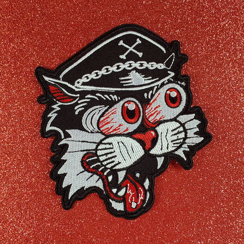 A black, white, and red embroidered patch of a biker cat with bulging cartoony bloodshot eyes, a chain-embellished biker cap, and wide open mouth 