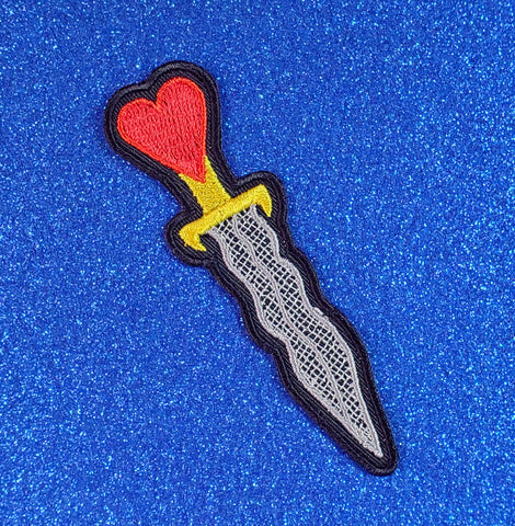 An embroidered black twill patch of an athame with a grey blade, gold handle, and red heart detail at the base