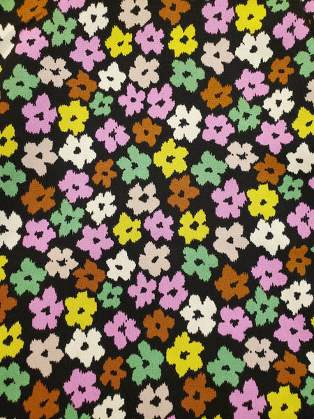 black background magenta, pale pink, green, brown, chartreuse, beige, and cream stylized flower print fabric swatch close up