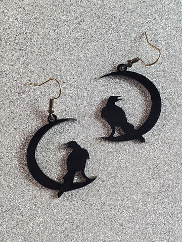 Laser cut acrylic dangle earrings in the shape of a crow perched on a crescent moon. Shown laying flat