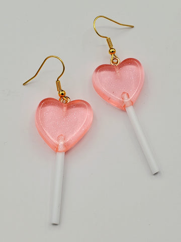 pair of acrylic dangle earrings with charms in the shape of translucent light pink heart-shaped lollipops with white plastic sticks