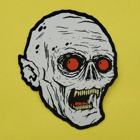 woven patch of a white vampire with pointy ears, red eyes, and yellow teeth