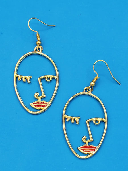 Gold metal dangle earrings with charms in the shape of abstract sketched faces with a winking eye and red enameled lips