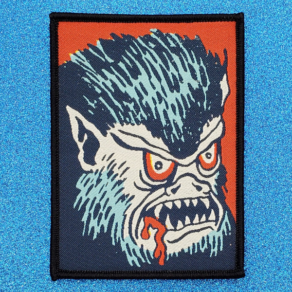rectangular woven patch with a black embroidered border featuring a cartoony blue and red wolf with bloody mouth