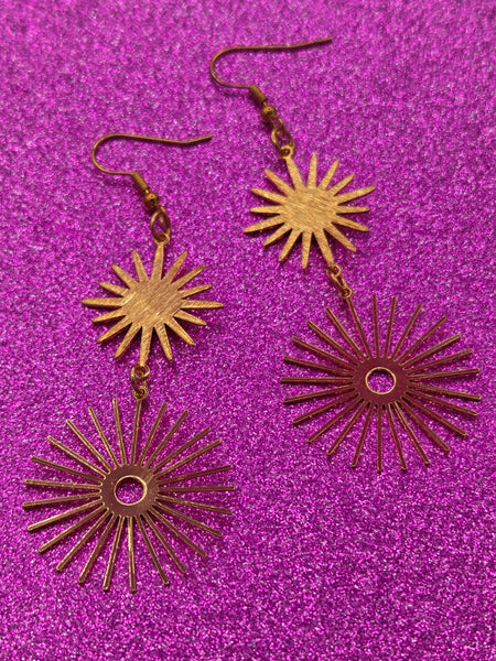 A pair of gold metal dangle earrings with two large starbursts -one smaller with solid middle and larger with hollow middle