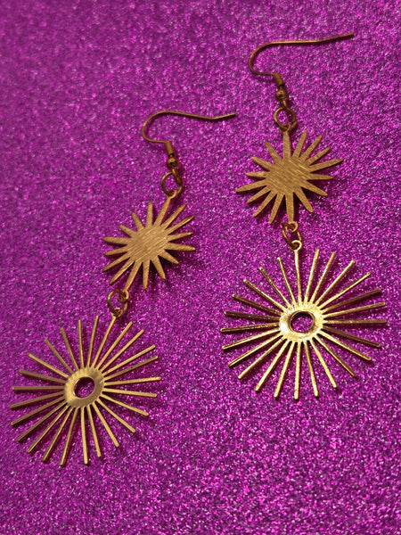 A pair of gold metal dangle earrings with two large starbursts -one smaller with solid middle and larger with hollow middle
