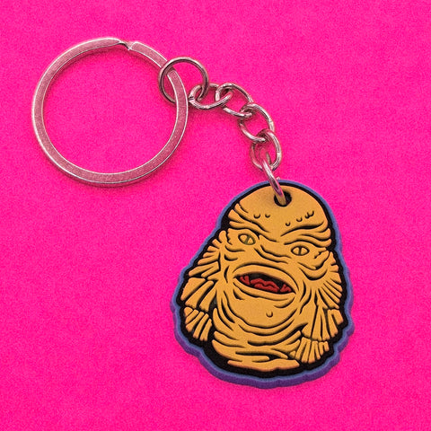 yellow, red, and blue Creature of the Black Lagoon PVC keychain with silver metal split ring, shown against bright pink background