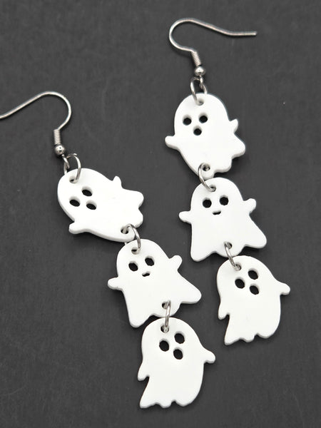 pair of dangle earrings, each comprised of three graduated size shiny white laser-cut acrylic cartoon ghosts linked together in a line