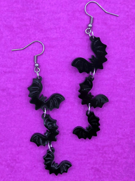 pair of dangle earrings, each comprised of three graduated size shiny black laser-cut acrylic bats linked together in a line