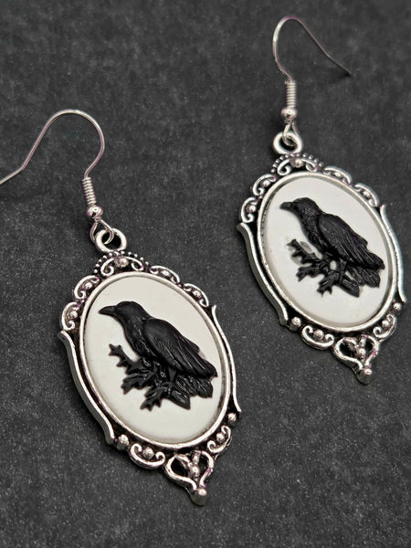 Silver metal cameo earrings with black silhouette of a raven on a white background