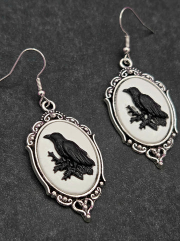 Silver metal cameo earrings with black silhouette of a raven on a white background