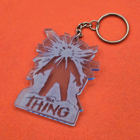 Laser-cut light blue acrylic keychain with etched detail of movie poster for The Thing shown on black background