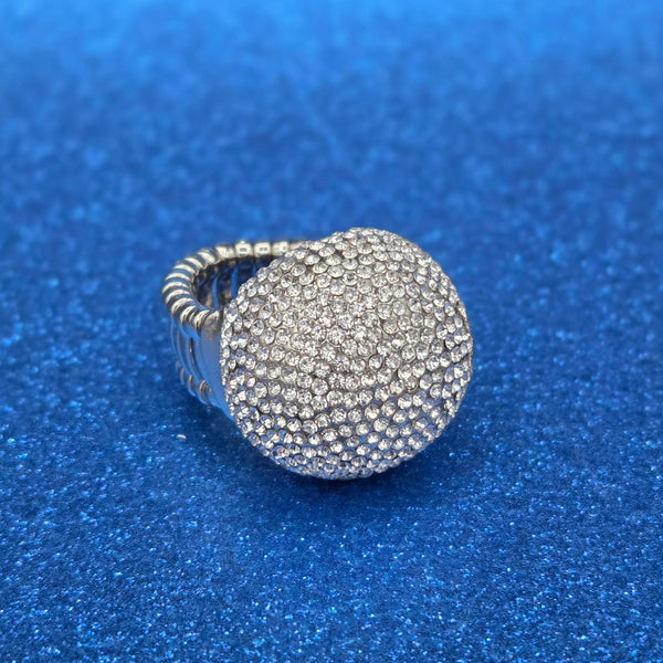 Silver metal cocktail stretch ring with large round bauble covered in clear rhinestone style jewels. shown 3/4 view