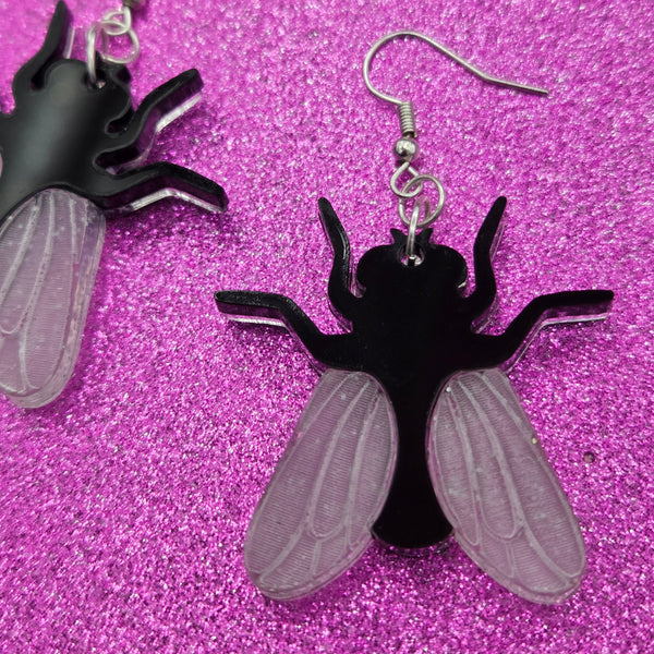 pair of laser cut acrylic earrings in the shape of house flies with black bodies and matte white etched wings