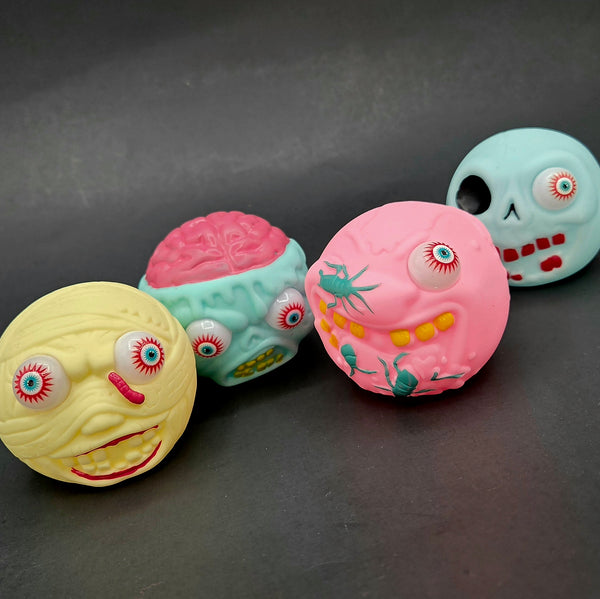 Four colorful rubber ball toys with face designs on a dark surface