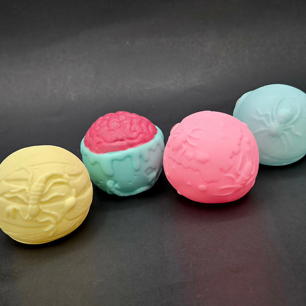 Four bug-textured balls in yellow, pink, and green on a dark surface