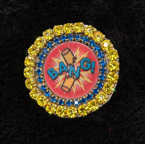 round lenticular dynamite/'BANG!' brooch with colorful rhinestone border, shown on a black background