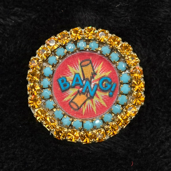 round lenticular dynamite/'BANG!' brooch with colorful rhinestone border, shown on a black background