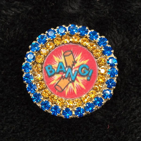 round lenticular dynamite/'BANG!' brooch with colorful rhinestone border, shown on a black background