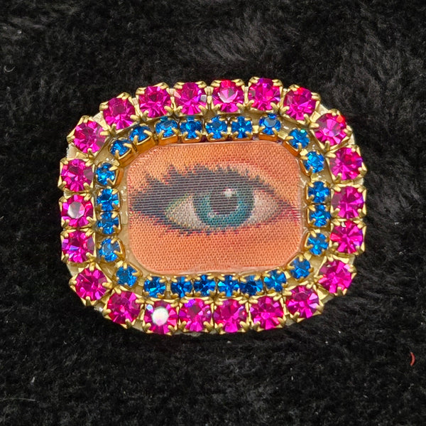 rectangular brooch with lenticular winking eye design and colorful rhinestones border, shown on a black background
