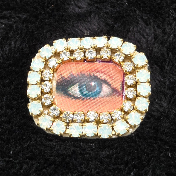 rectangular brooch with lenticular winking eye design and colorful rhinestones border, shown on a black background