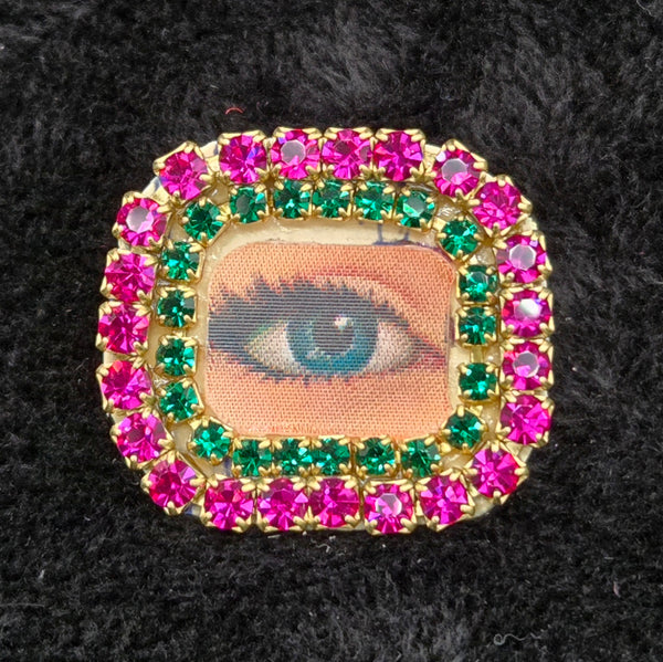 rectangular brooch with lenticular winking eye design and colorful rhinestones border, shown on a black background
