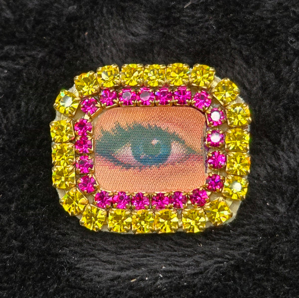 rectangular brooch with lenticular winking eye design and colorful rhinestones border, shown on a black background