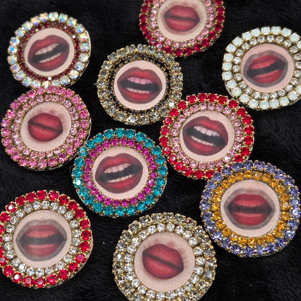 round brooches with lenticular lip designs and rhinestone embellishments on a black background