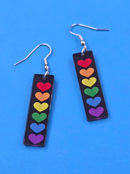 Pair of dangle earrings with acrylic rainbow heart charms on a blue background