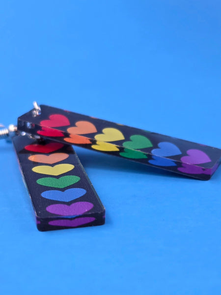 Pair of earrings with rainbow heart design on a blue background
