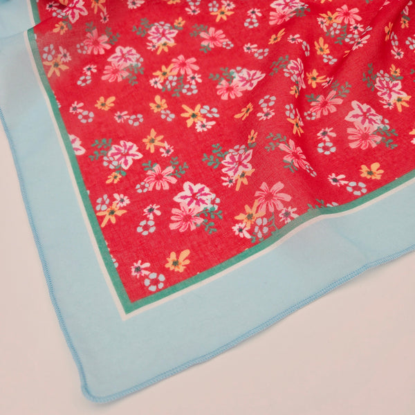 close up corner of red floral cotton blend square scarf with blue, white, and green border