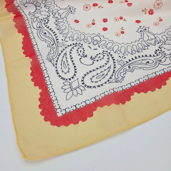 close up corner of square scarf with white background red and white dainty floral pattern with black outline paisley details and yellow & red scallop border