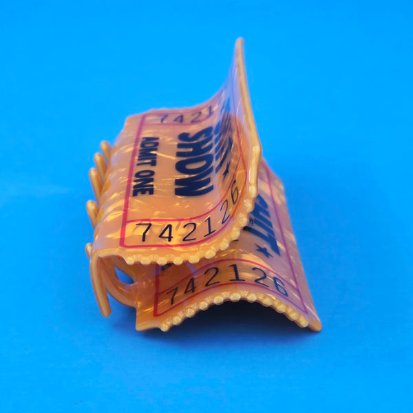 yellow marbled acetate ticket-shaped claw style hair clip with printed detail of "SHIT SHOW ADMIT ONE" shown end view