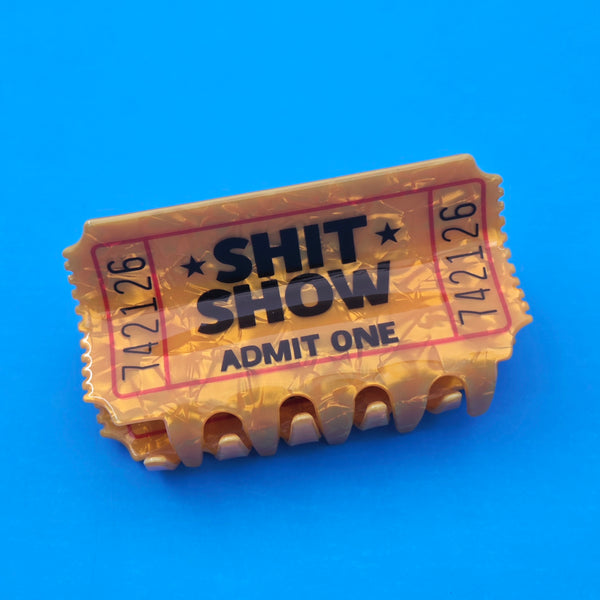 yellow marbled acetate ticket-shaped claw style hair clip with printed detail of "SHIT SHOW ADMIT ONE"
