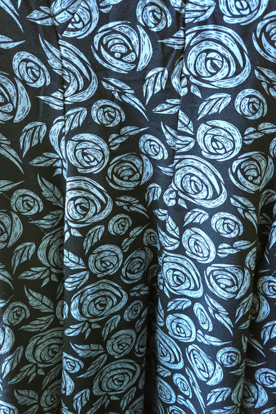 A close-up of a black fabric with a repeating hand-drawn style light blue rose and leaf pattern.